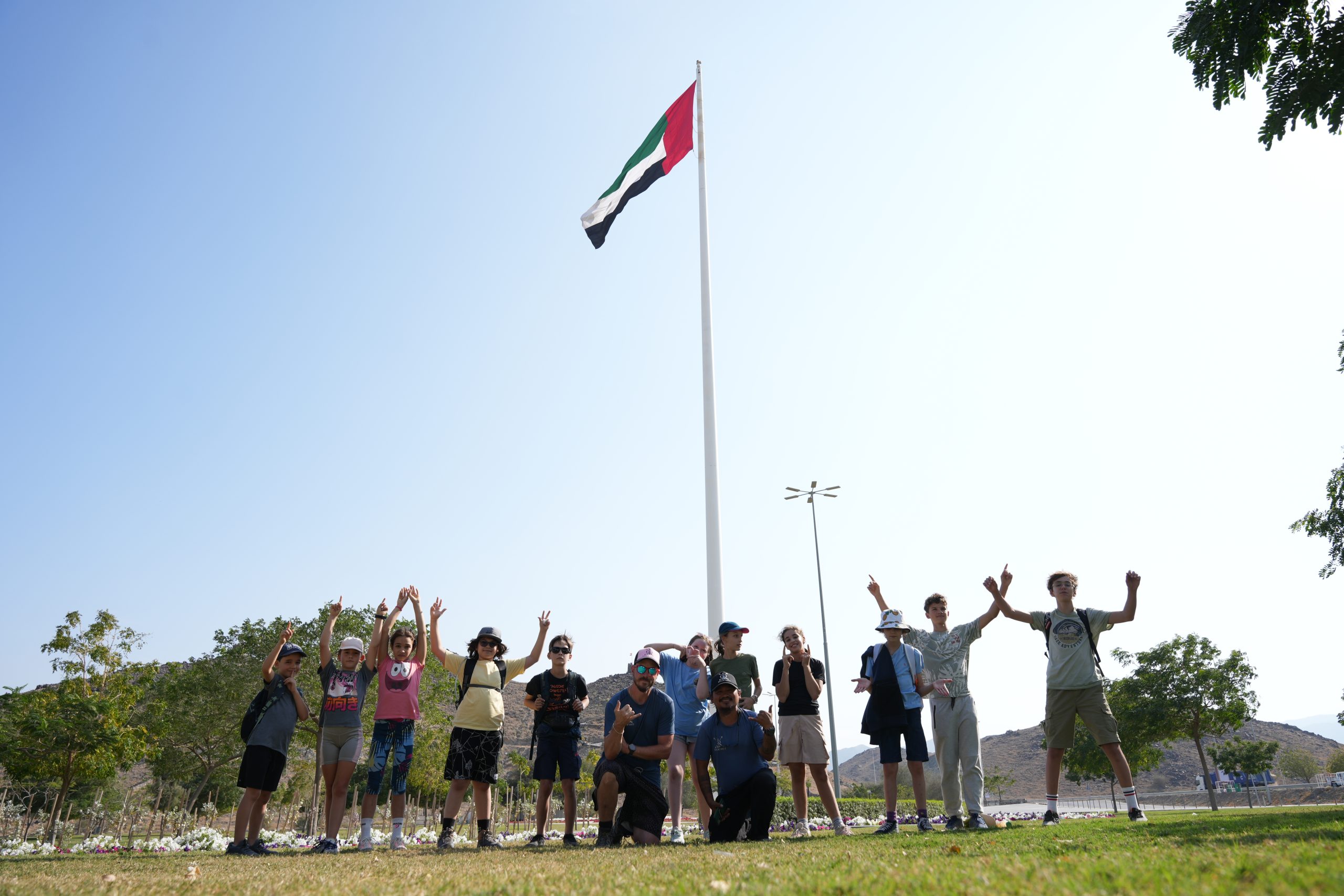 Group of people cheering under a UAE flagpole on a sunny day.