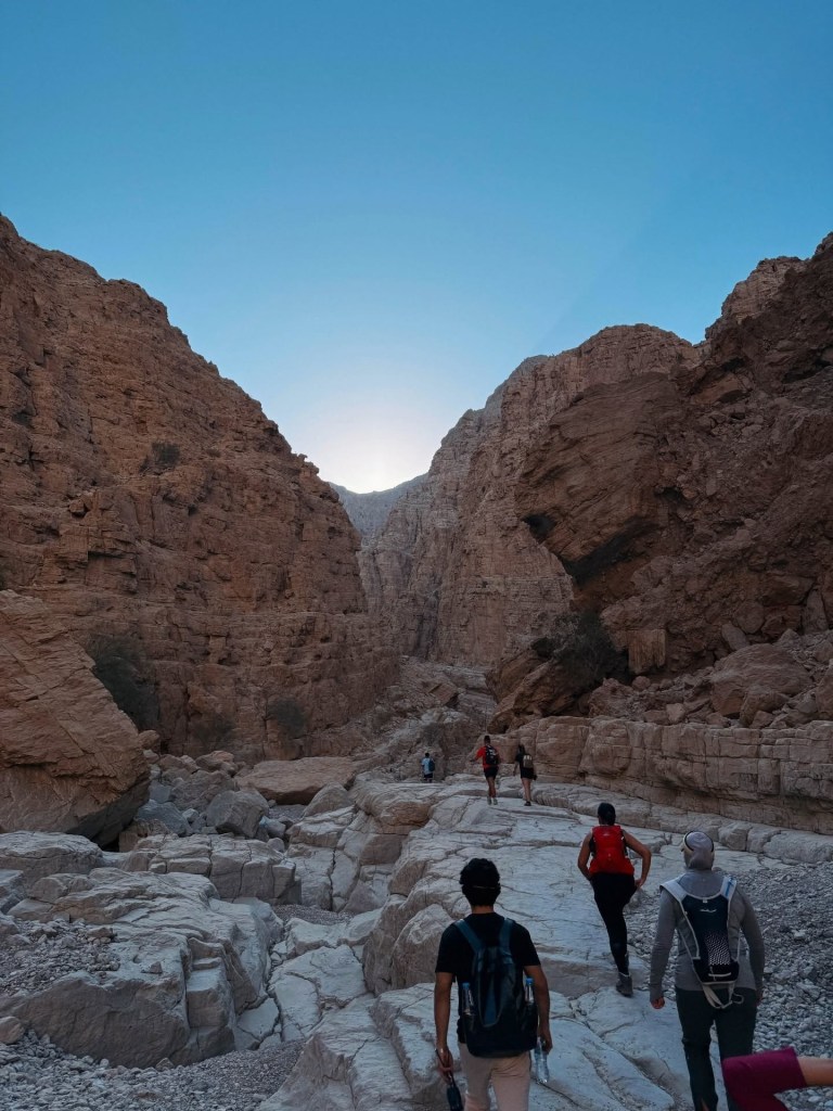 Hikers walk through rocky canyon with clear blue sky.