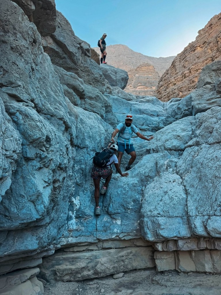 Three hikers climbing rocky terrain in a canyon under a clear sky.