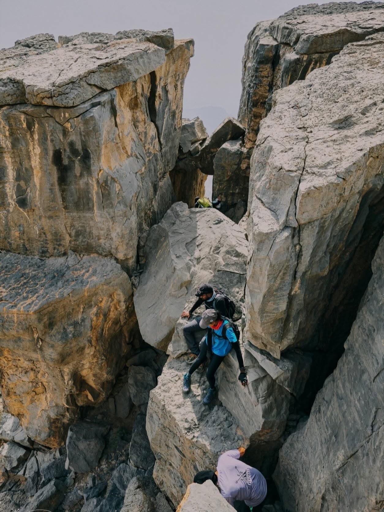 Three people climbing large rocky boulders in a narrow ravine.