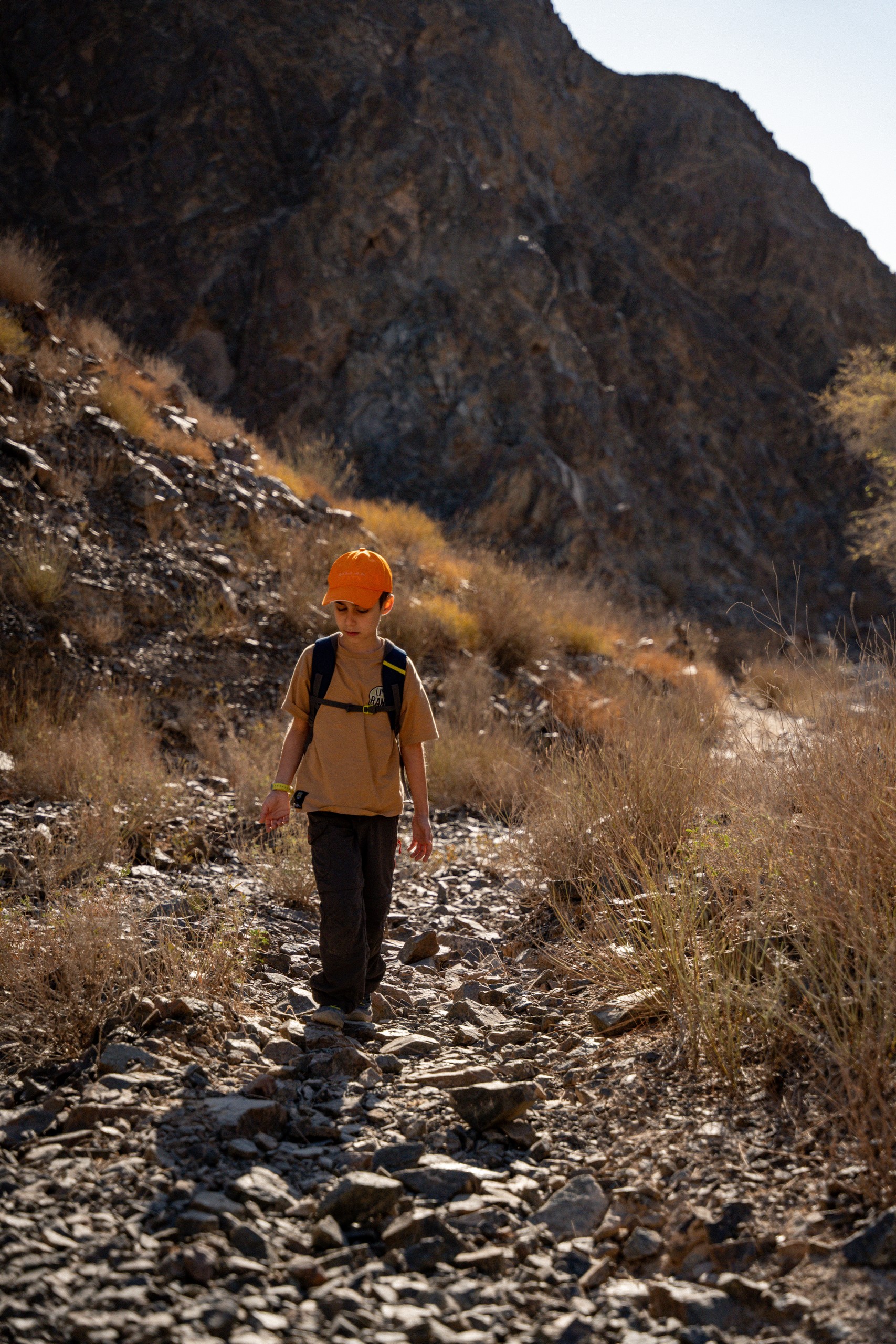 Child hiking alone on rocky mountain trail under clear sky.