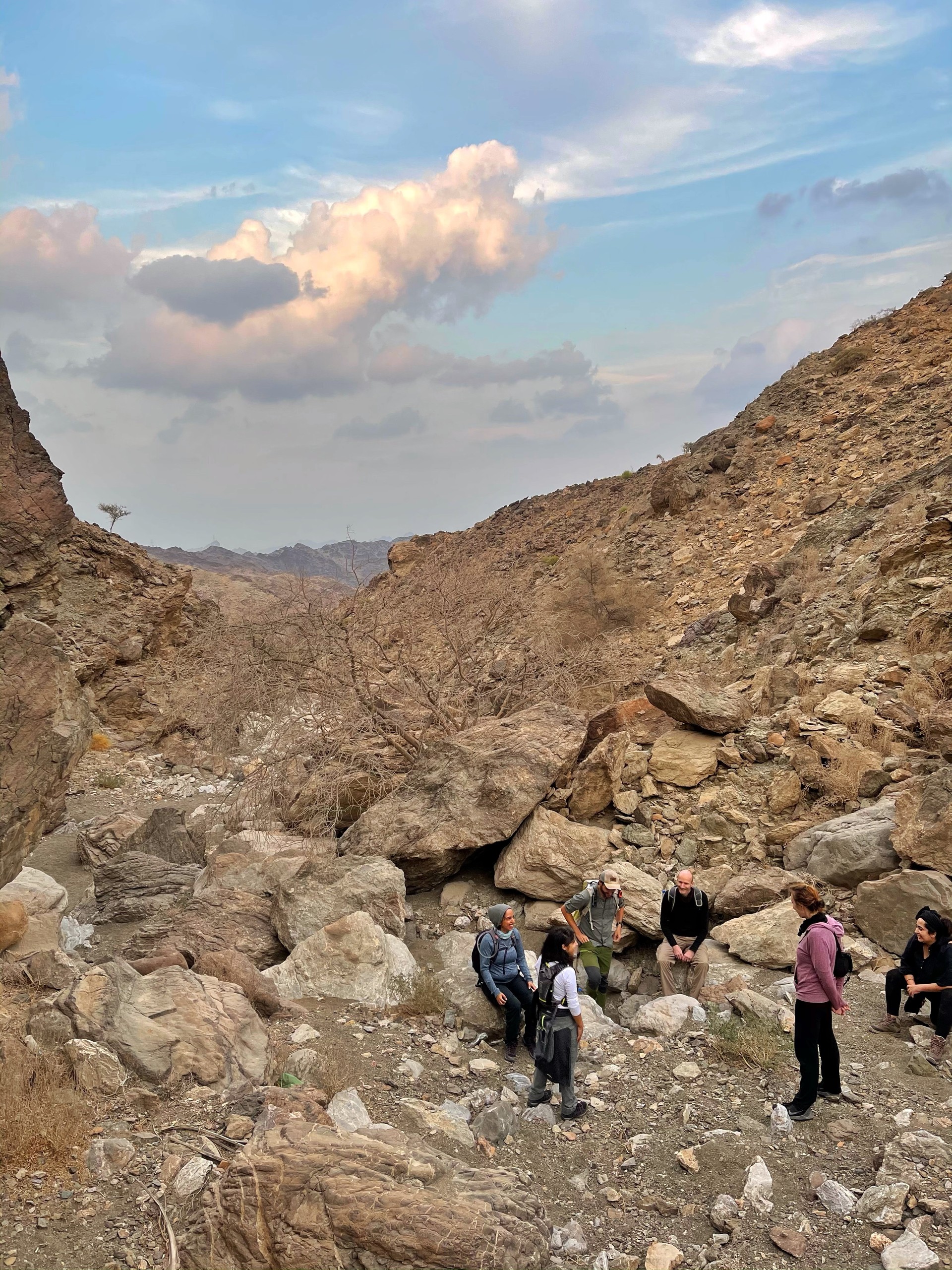 Group resting among rocks in a mountain landscape with cloudy sky.