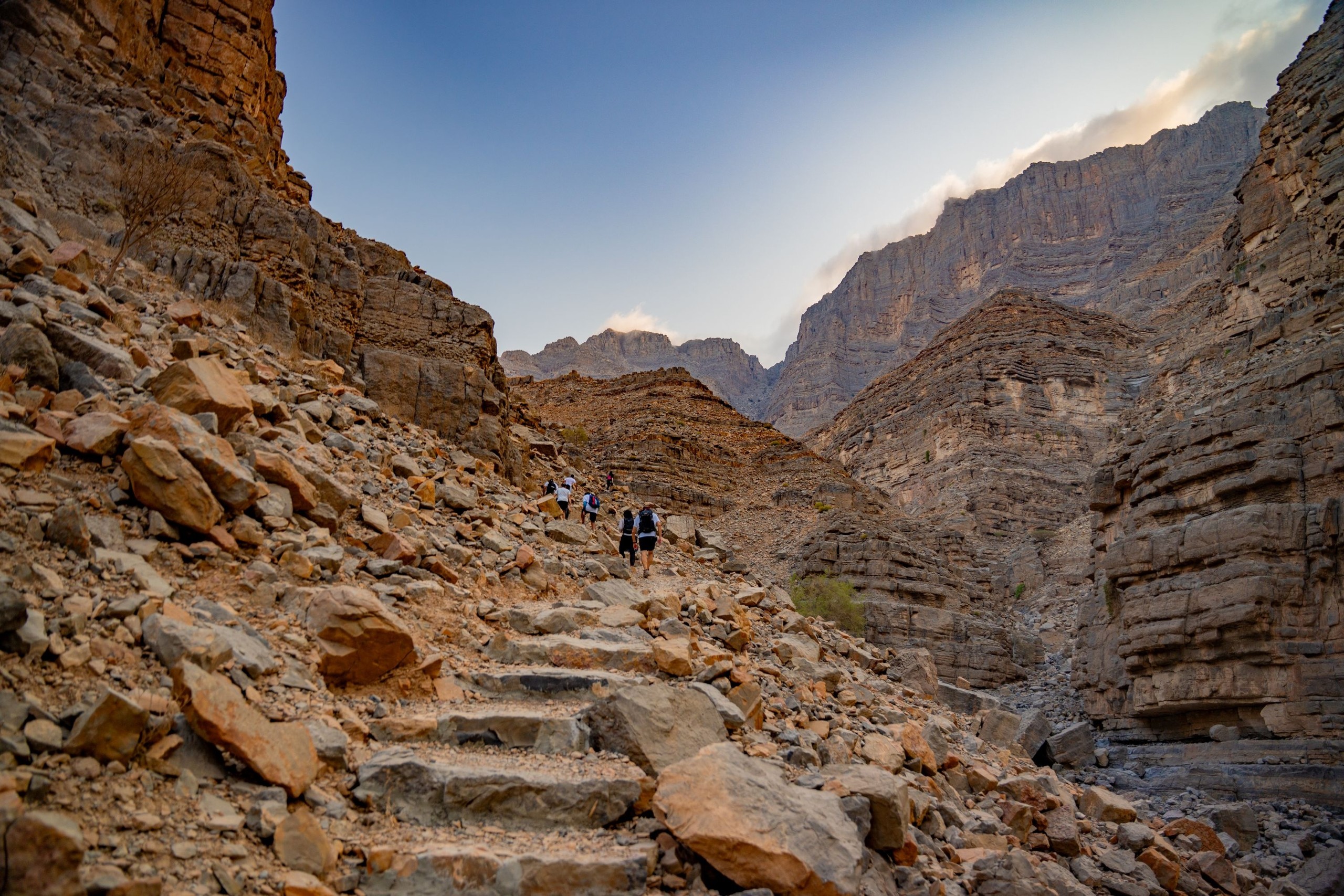 Hikers ascending rocky mountain trail at dusk.