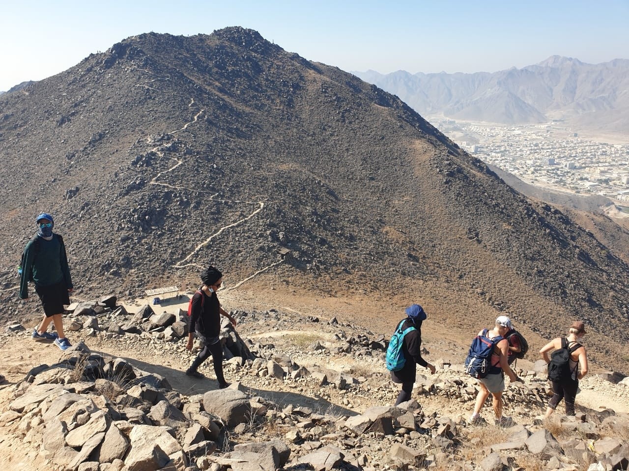 People hiking on a rocky mountain trail with a city view.