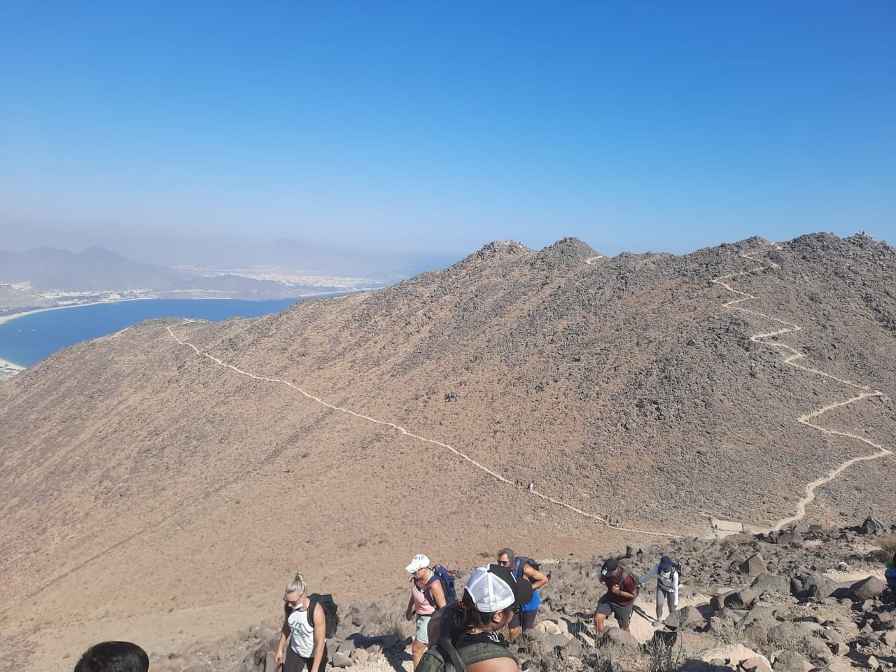 People hiking on a rocky mountain trail with a bay view.