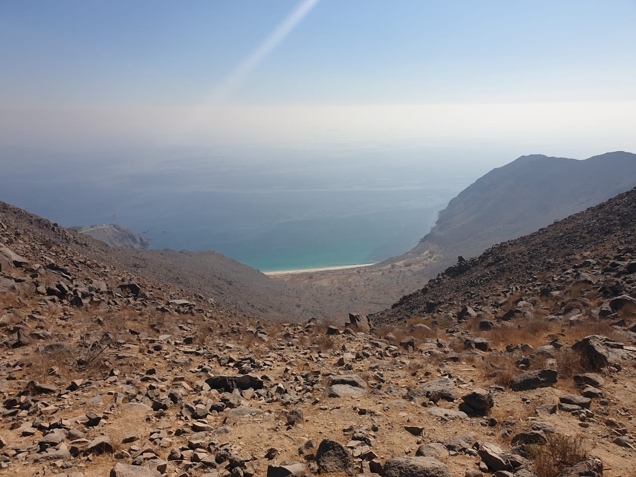 Rocky mountain slope leading to a beach, with sea and sky in the background.