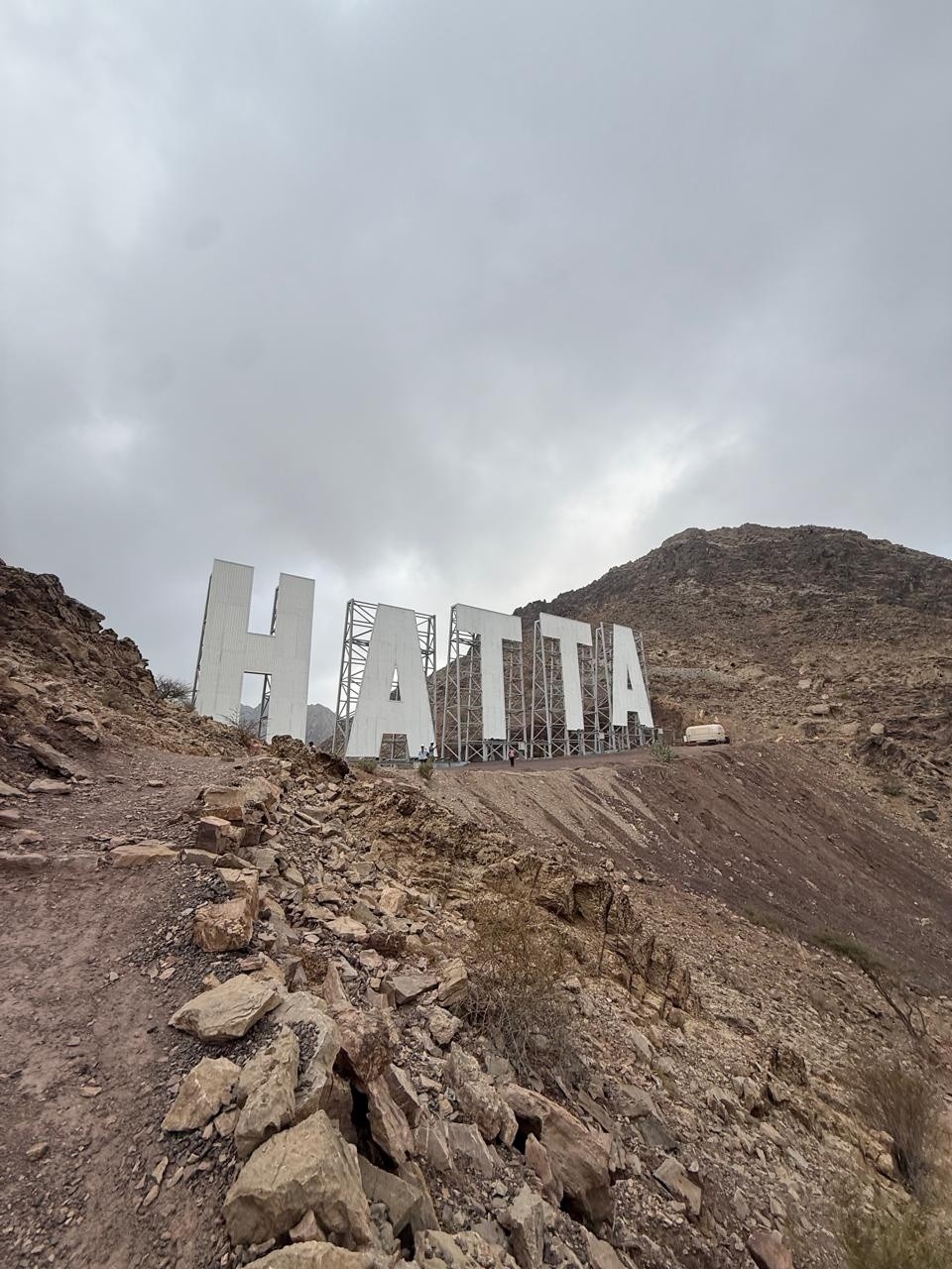 Large white 'HATTA' sign on rocky hillside under cloudy sky.
